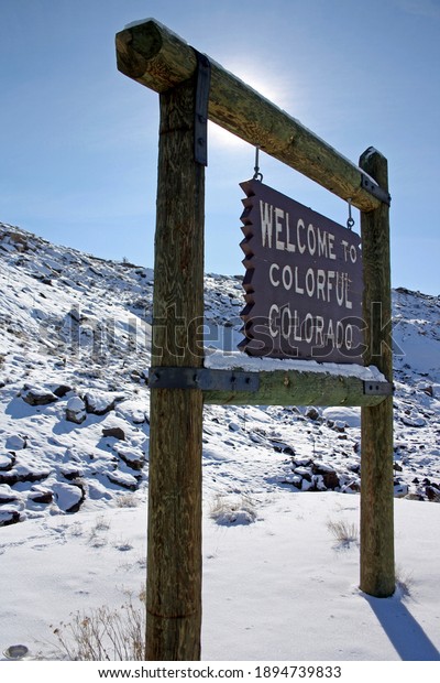 Colorado state sign during winter  with snow on\
the ground and blue\
skies.