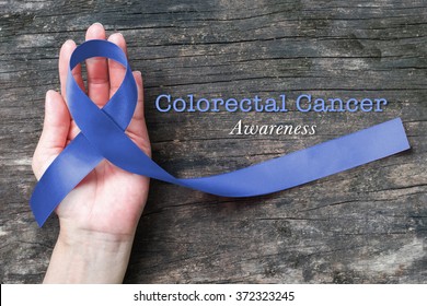 Colorectal Or Colon Cancer Awareness Dark Blue Ribbon On Helping Hand On Old Aged Wood