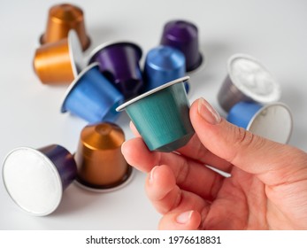 colored aluminum capsule with ground coffee in hand. White background with other capsules lying on it. Modern methods of making coffee. Capsule for coffee machine