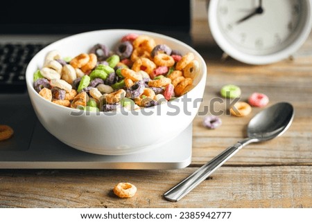 Colored breakfast cereals in a bowl and laptop, workplace breakfast, quick healthy breakfast in the office in the morning.