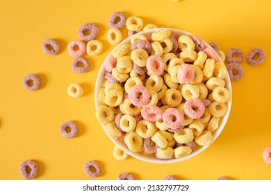 colored breakfast cereals laid out in a bowl on a yellow background top view, children's healthy breakfast cereals laid out in the shape of a smiley face