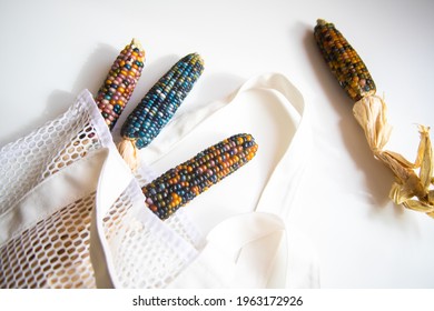 Colored Bright Corn In A Shopping Mesh Bag. Fancy Food, Dry Popcorn Product. White String Bag On A White Table On A Bright Sunny Day.
