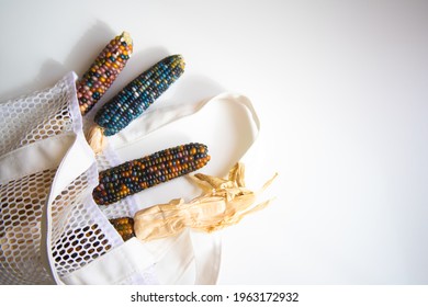 Colored Bright Corn In A Shopping Mesh Bag. Fancy Food, Dry Popcorn Product. White String Bag On A White Table On A Bright Sunny Day.
