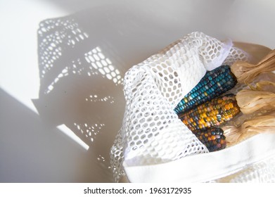 Colored Bright Corn In A Shopping Mesh Bag. Fancy Food, Dry Popcorn Product. White String Bag On A White Table On A Bright Sunny Day.
