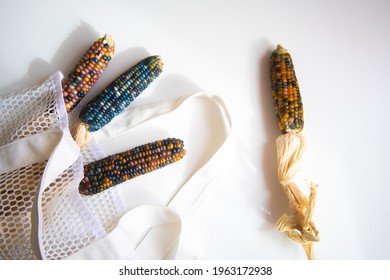 Colored Bright Corn In A Shopping Mesh Bag. Fancy Food, Dry Popcorn Product. White String Bag On A White Table On A Bright Sunny Day.
