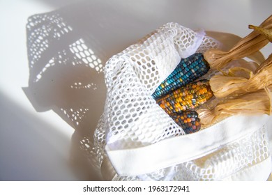 Colored Bright Corn In A Shopping Mesh Bag. Fancy Food, Dry Popcorn Product. White String Bag On A White Table On A Bright Sunny Day.
