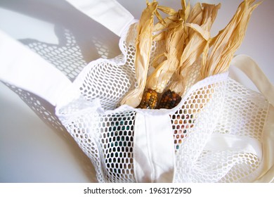 Colored Bright Corn In A Shopping Mesh Bag. Fancy Food, Dry Popcorn Product. White String Bag On A White Table On A Bright Sunny Day.
