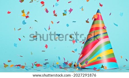 Colored confetti and party hat on blue background, happy birthday concept.