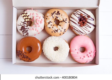 Colored donuts with glaze in a box on a white wooden background