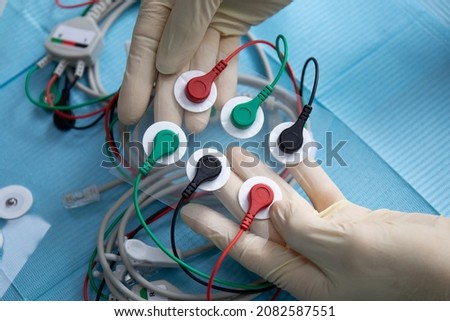 Colored electrodes, wires, hands in white gloves. Muscle neurostimulation.