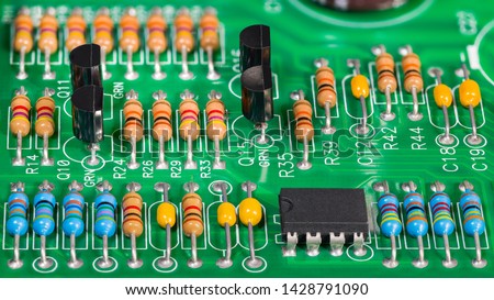 Colored electronic components. Resistors, transistors, capacitors and integrated circuit on PCB. Standard color code. Green copper board detail. Dismantled computer hardware. Electrotechnics, e-waste.