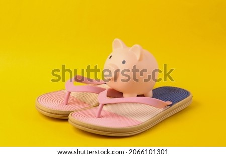 Colored flip flops with piggy bank on yellow background. Beach vacation concept. 