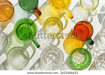 Colored Glasses pattern with shadow and sunlight reflection on white background, minimal aesthetic top view summer still life, refraction at shine drink, caustic effect, green yellow glass cups