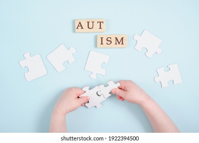 Colored Kids Hands Hold Puzzles On Blue Background, Autism Symbol, Autism Diagnosis Concept, Inscription Autism On Wooden Dominoes