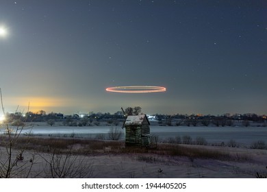 Colored lines over an old mill in a snowy field at night. Starry sky. Light graffiti