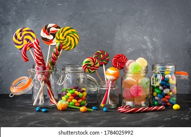 Colored lollipops, colorful round candies and marmalade in glass jars on a black stone table with a gray backdrop. Selective focus. Festive background with sweets - Powered by Shutterstock