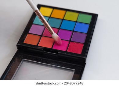 Colored Makeup Palette Lies On The Table. The Brush Held By The Makeup Artist Is Dipped To Pick Up Color