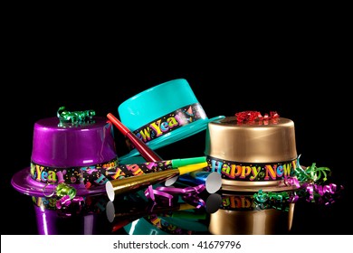Colored New Years Eve hats including green, purple, pink gold and red, streamers, noise makers and confetti on a black background
