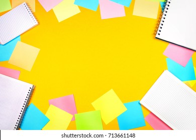 Colored note papers and various notepads with blank pages on a yellow background. Top view, copyspace.