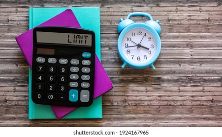 Colored notepads, alarm clock and calculator with display text LIMIT on wooden table