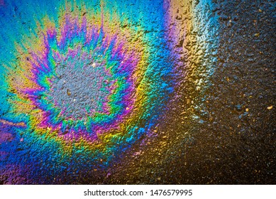Colored oil stain on the asphalt. A rainbow slick of gasoline. Abstract background.