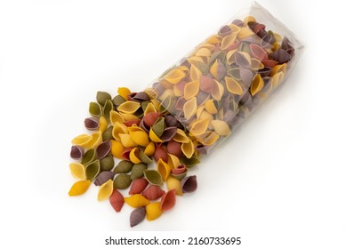 Colored pasta conchiglie (shells) that come out of transparent bag, italian durum wheat semolina pasta with turmeric, spinach, beetroot and black carrot isolated on white