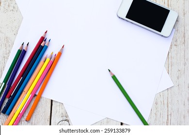 Colored Pencils, Cell Phone And Paper On The Desk