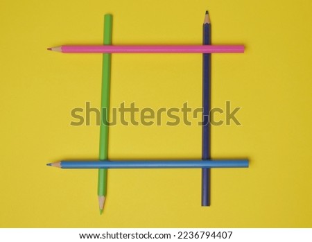 Colored pencils are laid out in the form of a tic-tac-toe game on a yellow background.
