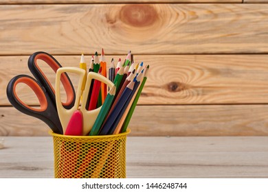 Colored pencils and scissors in basket. Wood color pencils in yellow metal pencil holder. Stationery items and drawing tools.