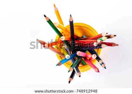 Colored pencils in yellow basket. Multicolored pencils in metal holder, top view.