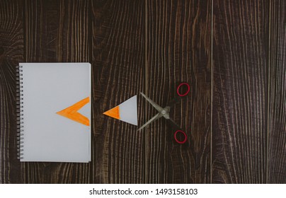 Colored plastic scissors with red handle after cutting a sheet of paper of a notebook lying on a wood background. free space for advertising text. top view