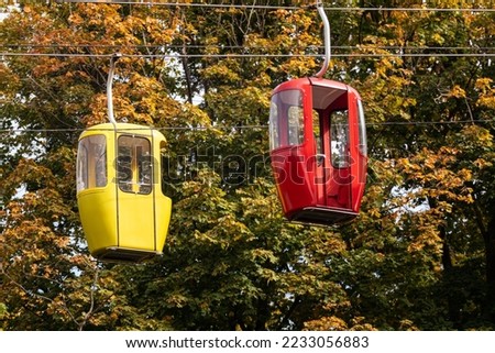 Colored red and yellow cableway cabins in autumn trees. Funicular transport on metal wires