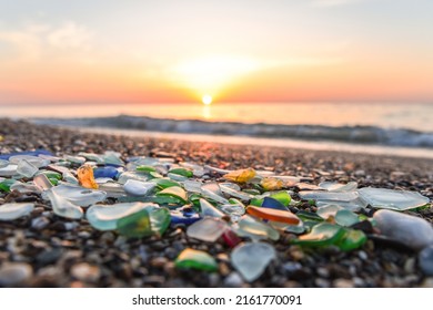 Colored sea glass with beach pebbles and shells in the mediterranean coast and in the background sea and waves with sunset and sky, sandy beach with coast glass, beach glass.