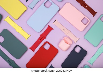 Colored Silicone Phone Cases, Complete With Watch Strap And Case For Headphones. Set. Up To Date Technology.Close Up Of Diverse Personal Accessory Laying On The Lavender Background. Flat Lay