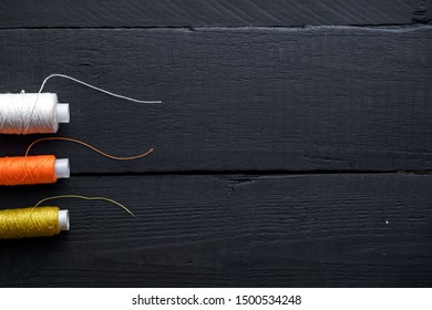Colored spools of thread for sewing on a wooden black background. Copy space 
