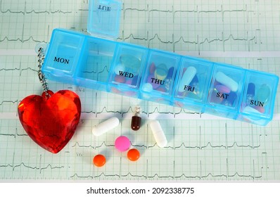 Farbige Tabletten aus einer Tablettenkiste mit rotem Herzen auf einer Kette und einem Elektrokardiogramm. Konzept der Gesundheitsversorgung.