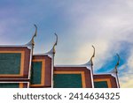 Colored temple Rooftop, Wat Suthat, Bangkok, Thailand. Blue, orange and green tiles. Ornate decorations. Blue sky and clouds in background.
