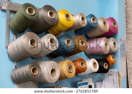 Colored thread spools on wall rack in sewing workshop