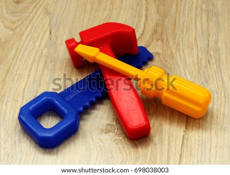 Colored toy plastic tools hammer, saw and screwdriver, lying on a wooden surface