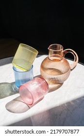 Colored Transparent Jug Of Water And Glasses On Table With Shadows. Utensils Flat Lay. Minimalism Style. Home Comfort. Objects Composition Idea