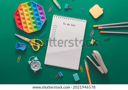 Colored various school supplies and an alarm clock on a green paper background. Back to school and education concept. Flat lay, top view, copy space. School plan and to do list.