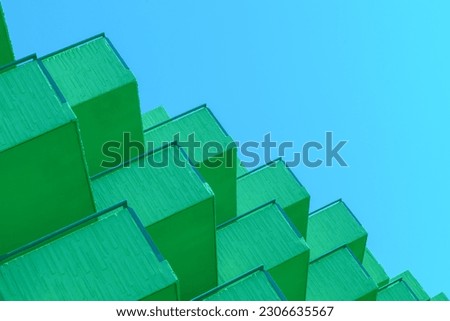 Colorful abstract architecture detail,  green shades against a blue sky. many balconies details of a modern architecture building seen below that create a repetitive geometric pattern. boxes blocks. 