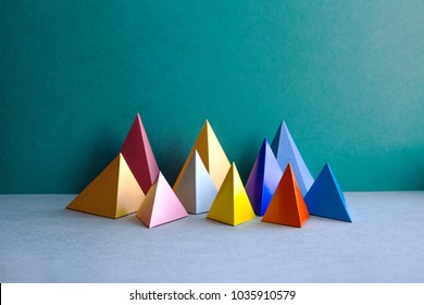 Colorful abstract geometric figures. Three-dimensional pyramid rectangular objects on green gray background. Yellow blue pink violet red colored tetrahedron Platonic solids background.
