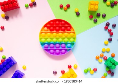 Colorful Anti-stress Pop It Toy Round Shape On A Colored Background, Top View. Candy Dragees Nearby