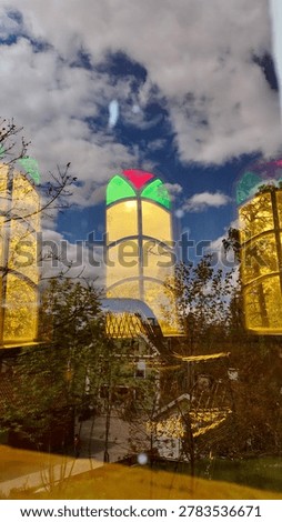 Colorful arched window with reflections of clouds and trees in dark glass. Decorative historic architecture detail with stained glass style and abstract outdoor reflections.