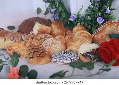 A colorful array of freshly baked breads and pastries, artfully arranged on a white surface, adorned with green leaves and a single red rose.