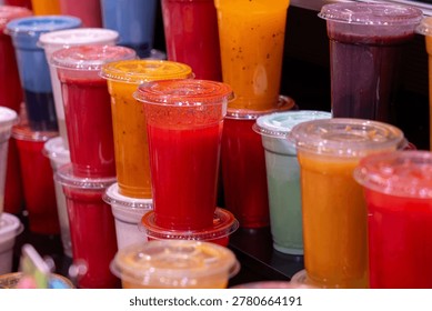 A colorful array of freshly squeezed fruit smoothies and juices in plastic takeaway cups displayed at a busy market stall.