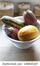 Colorful Assorted Winter Squash And Edirne Purple Striped Eggplants, Harvested At Early Autumn And Collected In White Bowl. Displayed In A Rustic Kitchen Background Of Wooden Surface And Straw Baskets