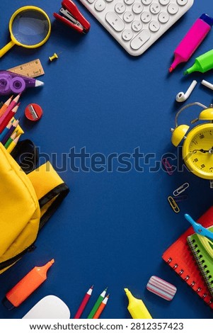 Colorful back to school flatlay featuring backpack, pencils, markers, alarm clock, notebook and other stationery items arranged on a blue background to convey study readiness and classroom preparation