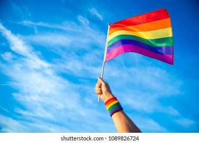 Colorful backlit rainbow gay pride flag being waved in the breeze against a sunset sky.